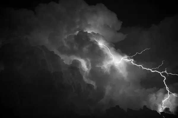Black and white photo of storm clouds with a bolt of lightning arching through them