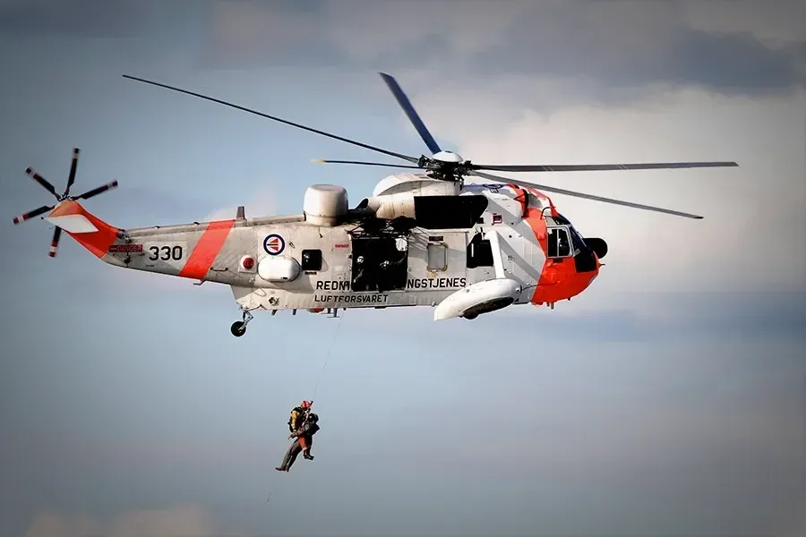 A rescue helicopter with two people dangling from a line suspended from it