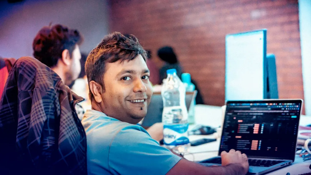 An engineer smiles over his shoulder from a laptop in a shared workspace