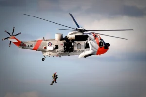 A rescue helicopter with two people dangling from a line suspended from it