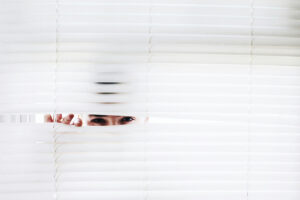 A person peaking through white blinds