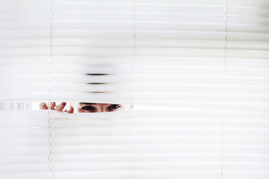 A person peaking through white blinds